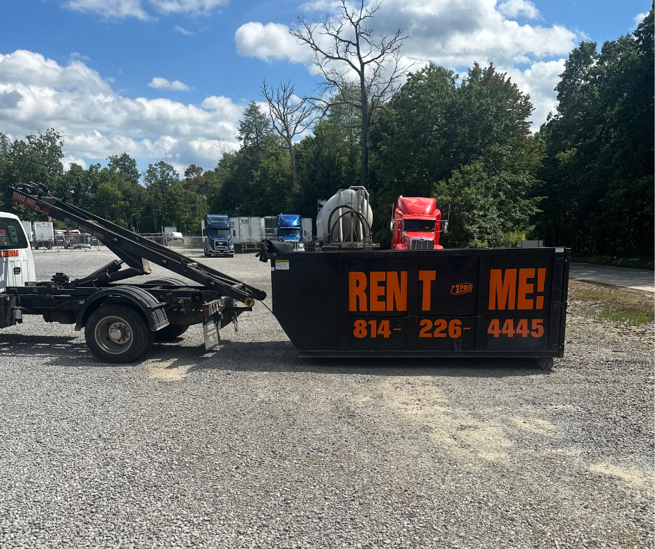 A side shot of a 15 yard dumpster with rent me on it in front of a red semi truck